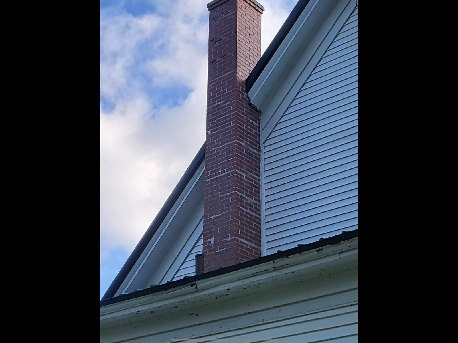 Completed brick chimney rising above house roof with cloudy sky in background
