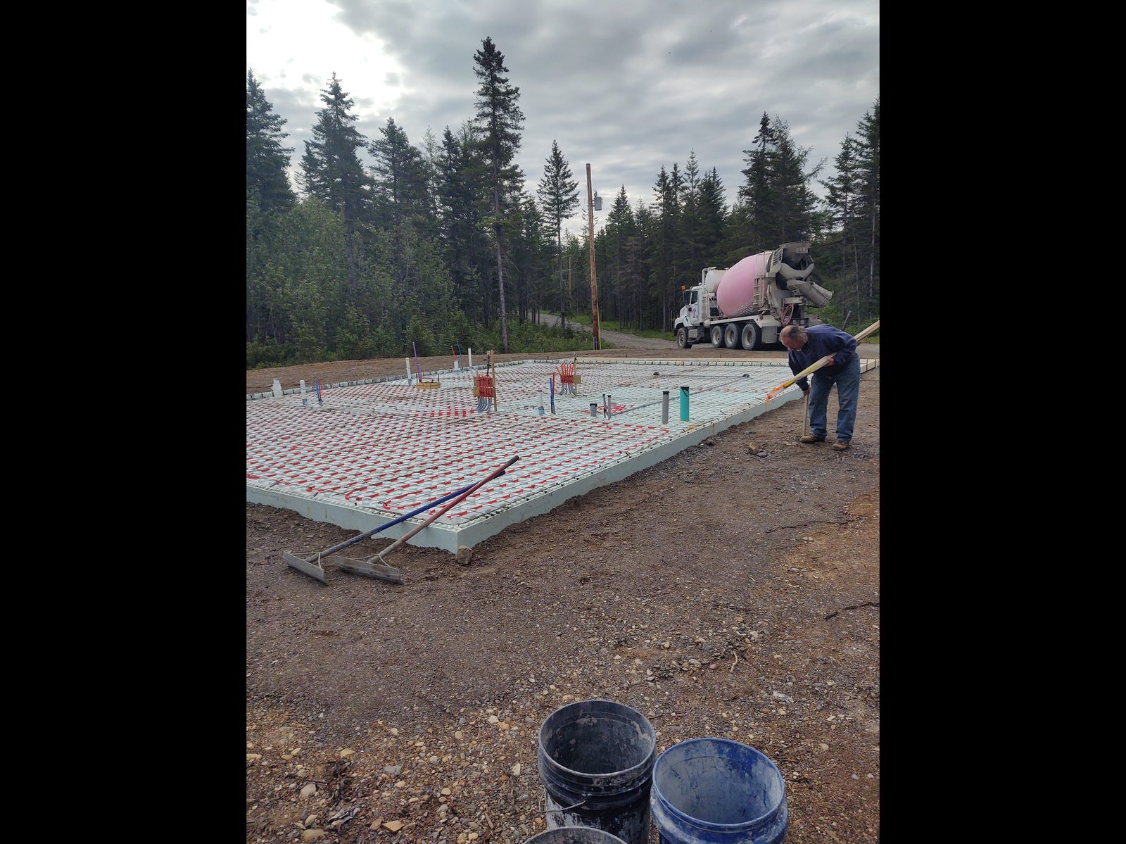 Concrete slab site preparation with radiant heat tubing and cement truck in background